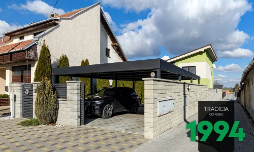 Auto pod přístřeškem za betonovým plotem
