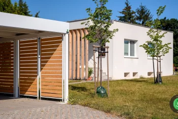 Přístřešek pro dvě auta s bílou střechou mezi stromy v zahradě