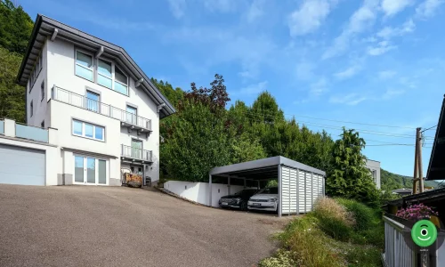 Přístřešek GARDEON vedle velkého bílého rodinného domu