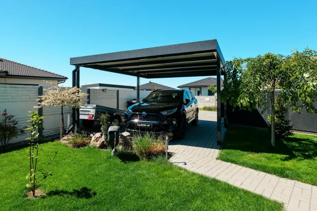 Prostorný přístřešek pro auto umístěný u upravené moderní zahrady