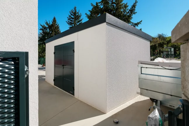 Minimalistický zahradní domek se zastřešeným prostorem vedle rodinného domu