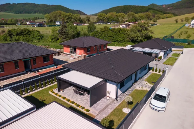 Letecký pohled na pergolu s plochou střechou u bílého rodinného domu, zelené okolí s horami
