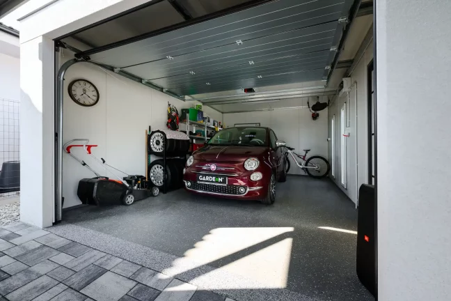 Interiér bílé garáže s otevřenými rolovacími vraty, červené auto a jízdní kolo uvnitř