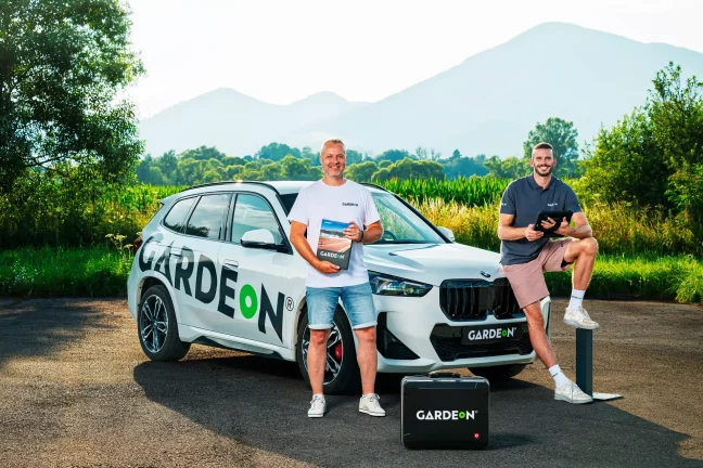 Dva agenti GARDEON s vzorníkem a tabletem u firemního BMW.