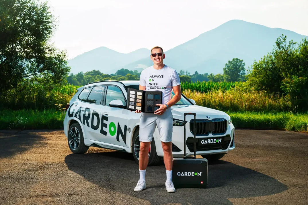 Obchodní agent drží vzorník omítek před firemním BMW v přírodě.