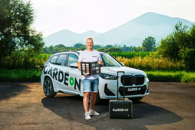 Usmívající se agent GARDEON se vzorníkem povrchů stojí u firemního BMW.