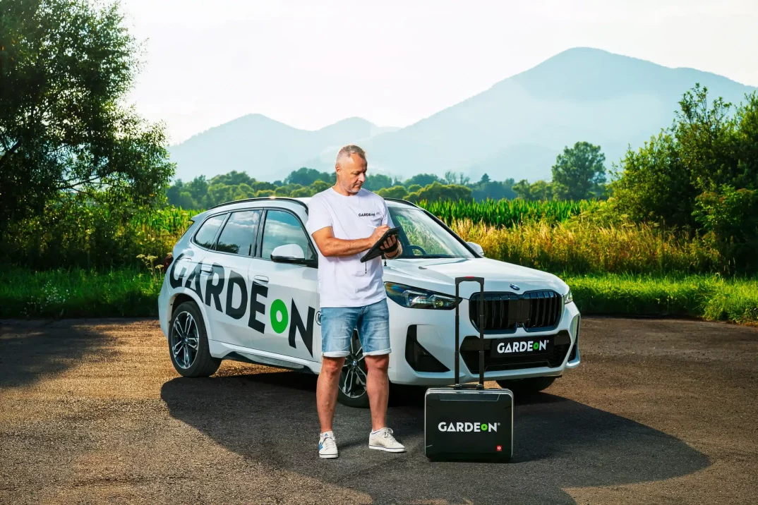 Agent GARDEON s tabletem, firemní BMW a kufřík v přírodě.