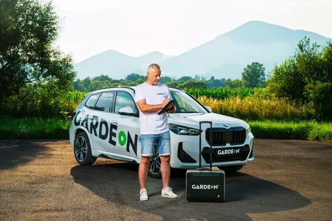 Agent GARDEON s tabletem, firemní BMW a kufřík v přírodě.