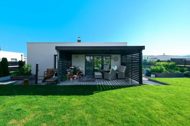 Antracitová pergola s kovovou výplní u rodinného domu s travnatou zahradou.