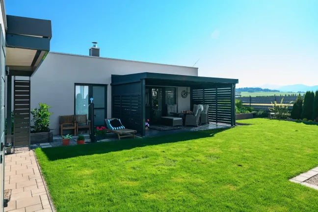 Antracitová pergola s kovovou výplní u rodinného domu se zahradou.