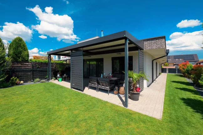 Antracitová pergola se zahradním posezením, pohled z boku na zelenou zahradu