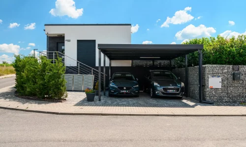 Přístřešek s antracitovou plochou střechou a bočním panelem u moderního domu.