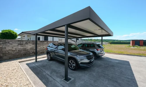 Plochá antracitová střecha přístřešku chrání dvě SUV u rodinného domu.