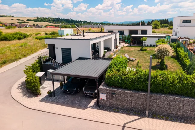 Vzdušný pohled na dvouprostorový přístřešek s antracitovou plochou střechou u moderního bungalovu.