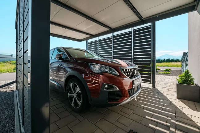 Přístřešek s antracitovou kovovou výplní s parkujícím SUV.