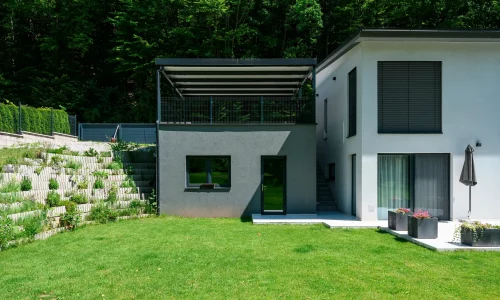 Antracitová pergola s pultovou střechou osazená na vyvýšeném podkladu