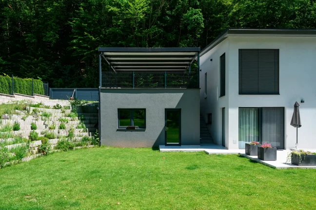 Antracitová pergola s pultovou střechou osazená na vyvýšeném podkladu