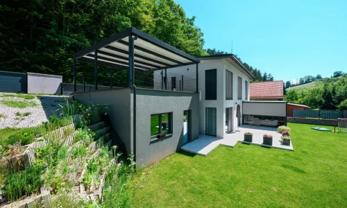 Pergola s antracitovou ocelovou konstrukcí a pultovou střechou u rodinného domu.