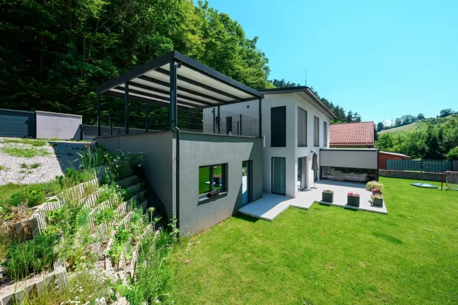 Pergola s antracitovou ocelovou konstrukcí a pultovou střechou u rodinného domu.