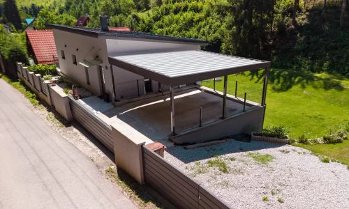 Vzdušný pohled na přístřešek s trapézovou střechou u bílého rodinného domu.