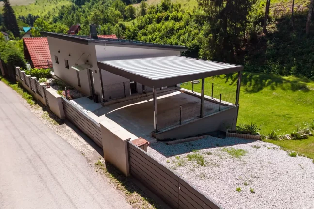 Vzdušný pohled na přístřešek s trapézovou střechou u bílého rodinného domu.