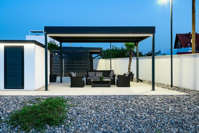 Večerní pergola s antracitovými ocelovými sloupky a ratanovým sezením v zahradě.