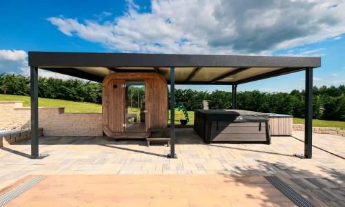Antracitová pergola s plochou střechou u sudové sauny na dlážděné terase, modrá obloha