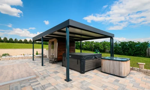 Antracitová pergola s vířivkou pod ní na dlážděné terase, zelená zahrada a modrá obloha