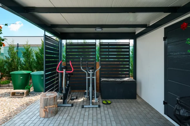 Fitness zóna pod antracitovým přístřeškem s kovovou lamelovou výplní bočních stěn.