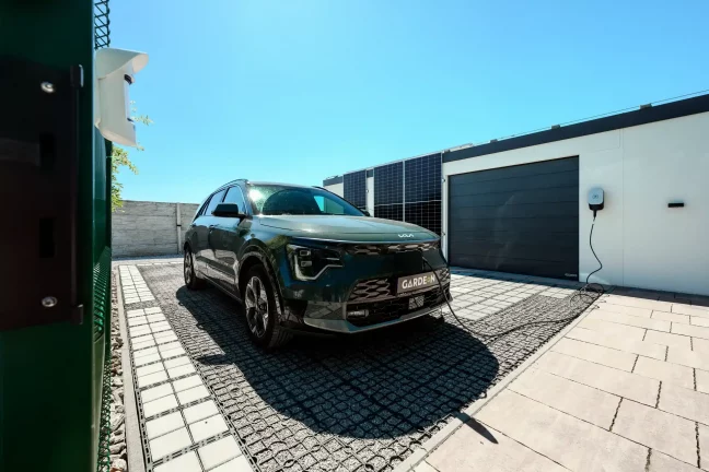 Zelené auto připojené k nabíjecí stanici u garáže