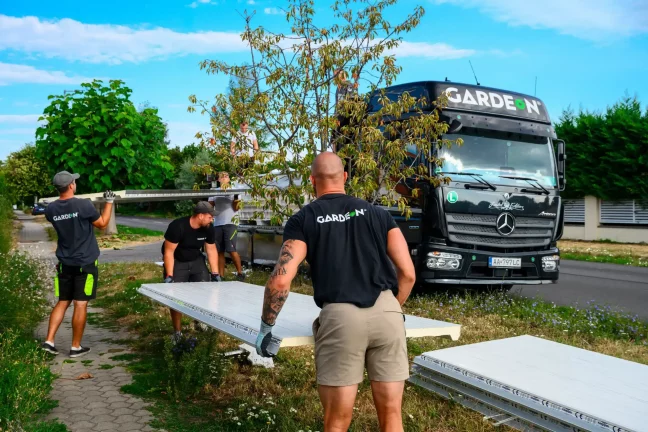Montážníci přenášejí bílé sendvičové panely od nákladního auta po trávě