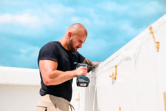 Detailní záběr pracovníka vrtajícího do bílé střešní lišty garáže