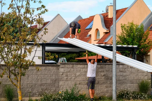 Pracovník podává bílý střešní panel kolegovi na střeše přístřešku
