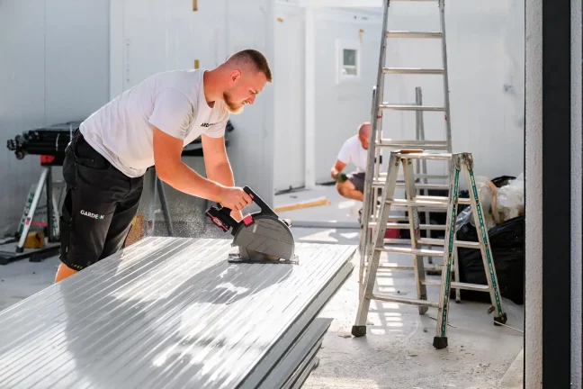 Pracovník řeže rozbrušovačkou střešní panel, kolem létají jiskry