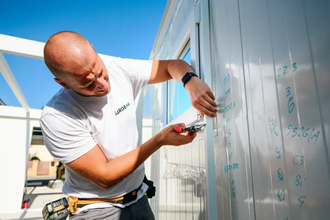 Pracovník zastřihuje nůžkami okraj bílého panelu u okenního rámu