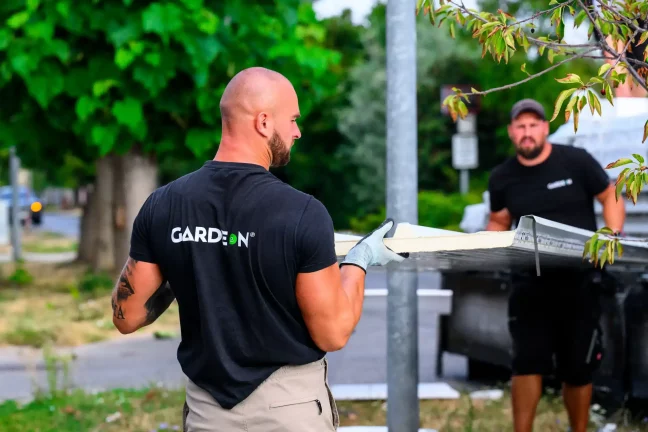 Dva pracovníci Gardeon společně nesou stěnový panel podél ulice