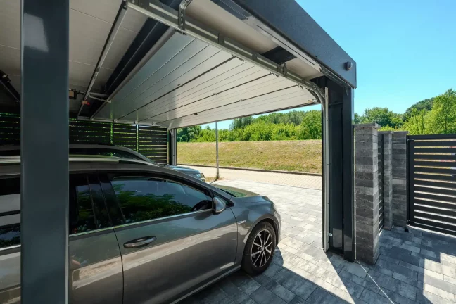 Pohled zpod přístřešku přes otevřená vrata na cestu