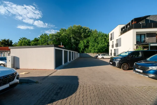 Řada garáží s parkovištěm, auty a bílým bytovým domem