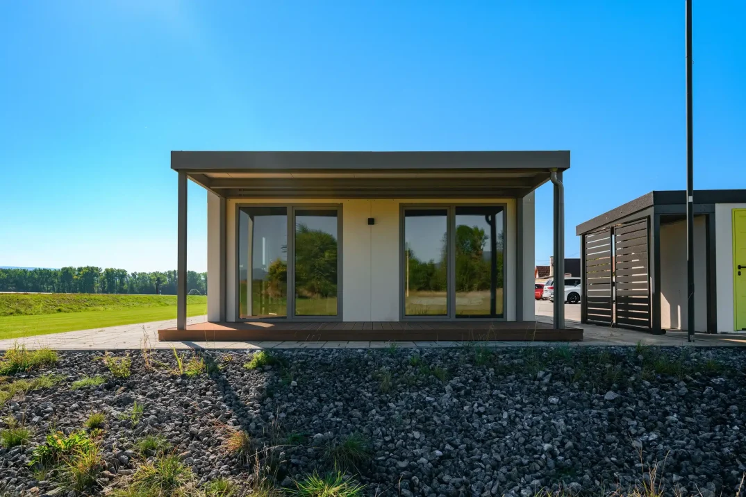 Tiny house zepředu s krytou dřevěnou terasou a posuvnými prosklenými dveřmi