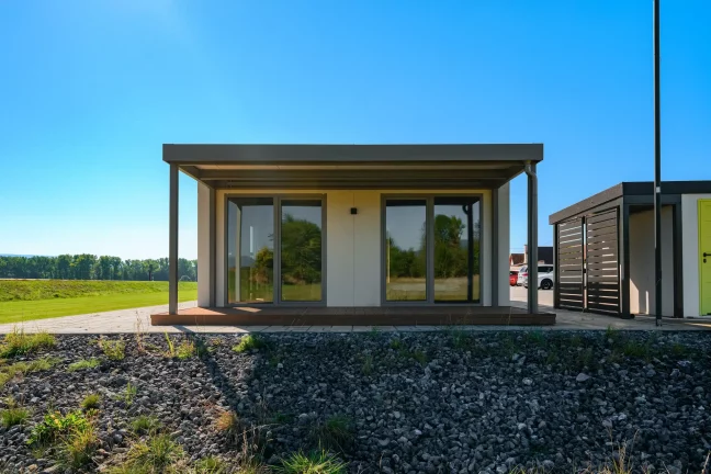 Tiny house zepředu s krytou dřevěnou terasou a posuvnými prosklenými dveřmi