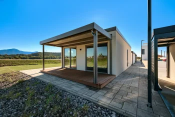 Krytá terasa tiny housu s výhledem na hory a dlážděným chodníkem podél domu