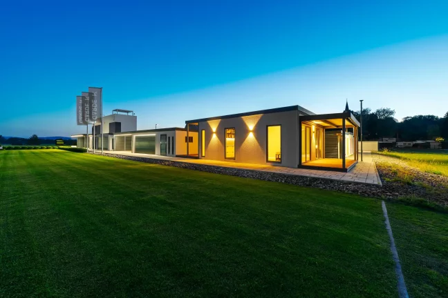 Osvětlený tiny house za soumraku, pohled z dálky přes trávník