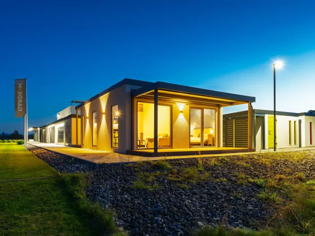 Přední roh osvětleného tiny housu s krytou terasou za soumraku