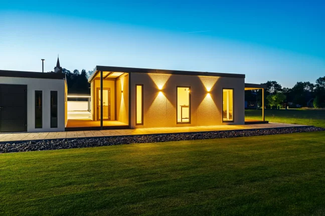 Boční stěna tiny housu s rozsvícenými nástěnnými světly večer